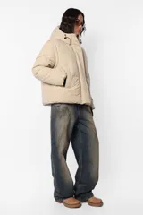 Campera puffer beige de corte oversize, confeccionada en textil impermeable. Cuenta con capucha forrada con tancas y elástico, cuello alto, cierre frontal con cartera y abrojo, bolsillos ribete con cierre, mangas desmontables con mitones y cintura ajustable con elástico y tancas. Incluye cinta gross estampada para transportarla al hombro y bolsillo interno con cierre invisible.