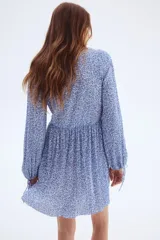 Vestido corto azul con estampado floral blanco, escote en V pronunciado con fruncido central, mangas globo largas con lazos ajustables en los puños y falda corta plisada.