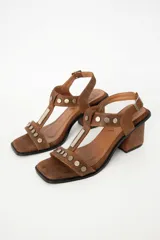 Sandalias marrones de cuero con taco cuadrado, tiras con apliques metálicos y hebilla lateral.