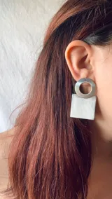 Aros colgantes con forma geométrica, hechos con guampa y detalles metálicos dorados o plateados.