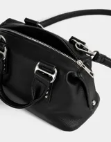 Cartera bowling negra de cuerina con tachas decorativas, doble asa de mano corta y correa regulable y desmontable.