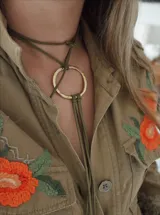 Gargantilla verde con dije circular dorado, confeccionada en bronce y cuero sintético.