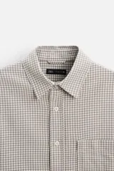 Camisa color crema de corte relaxed fit, confeccionada en tejido de mezcla de algodón suave al tacto. Tiene cuello solapa, manga larga con puños abotonados, un bolsillo de parche en el pecho y cierre frontal con botones.