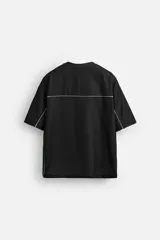 Camiseta negra de corte boxy fit, cuello redondo y manga corta. Presenta logos estampados en blanco en el frente y detalles en verde en los laterales.