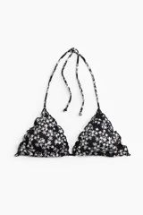 Top de bikini negro con estampado floral blanco, con copas triangulares con relleno extraíble y tiras finas para atar en la nuca y la espalda. Presenta costuras sobrehiladas con efecto de volados.