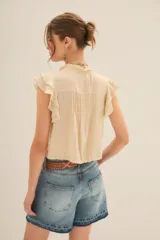 Camisa color crema de corte corto con escote redondo, mangas cortas con volados y jareta ajustable en el ruedo.