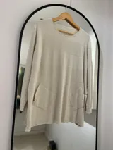 Sweater beige de punto con cuello redondo, manga larga y bolsillos delanteros.