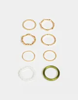 Set de 8 anillos dorados con diferentes diseños, uno de resina verde y uno de perlas blancas elásticas.