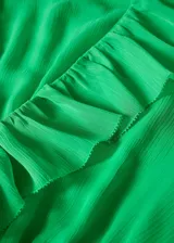 Vestido corto verde con textura, diseño evasé, cuello escotado con volantes, manga larga con puños elásticos, fruncido elástico en la cintura, volante en el bajo y cierre de lazo en el cuello.