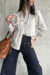 Camisa color beige de lino con detalles de broderie en el frente y mangas largas con puños elásticos.