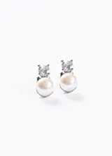 Par de aros tipo stud de plata 925, cada uno compuesto por una piedra zirconia engastada en cuatro puntas en la parte superior y una perla de río colgante en la parte inferior.