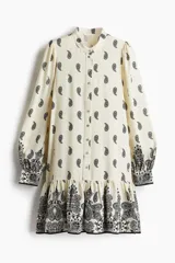 Vestido corto de viscosa color crema con estampado paisley en negro, cuello mao, botones frontales, mangas largas abullonadas con puños abotonados y falda con volantes.