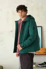 Campera con capucha de color verde oscuro, con cierre frontal y bolsillos con cierre en el pecho. Presenta puños ajustables y un parche con logo en la manga.