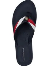 Ojotas de mujer color azul marino con tira de tela trenzada que presenta franjas rojas y blancas, y un dije metálico con el monograma TH en dorado.