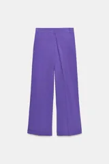 Pantalón negro de tiro alto con corte palazzo, bolsillos laterales y pliegues frontales. Cierre frontal con cremallera y botón.