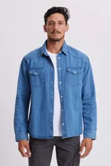 Camisa de jean celeste de manga larga con cuello clásico, cierre con botones a presión y dos bolsillos con solapa abotonada en el pecho.