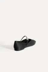 Zapato tipo bailarina color negro con efecto satinado, punta redonda y tira con hebilla ajustable.