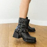 Bota corta negra de cuero con textura tipo piel de cocodrilo, caña media, punta cuadrada, taco de madera y estribo desmontable con hebillas.