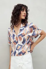 Camisa de manga corta con estampado de hojas blancas sobre fondo celeste, cuello solapa y botones de nácar al frente. Confeccionada en tejido liviano de sutil textura.