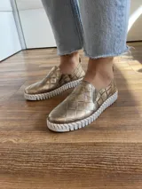 Zapatilla marrón de cuero con diseño entretejido, elástico lateral y suela blanca.