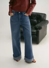 Pantalón de jean azul de corte wide leg, tiro medio, con cierre de cremallera y botón, bajo con dobladillo y cinco bolsillos.