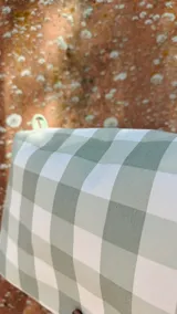 Necessaire rectangular de tela estampada a cuadros verdes y blancos, con cierre superior y etiqueta verde con logo.