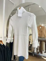 Polera blanca de tejido de punto acanalado, con cuello alto y mangas largas con puños acampanados.