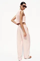 Pantalón de vestir color rosa pálido, de tiro alto, con pinzas delanteras, bolsillos laterales, pierna ancha y cierre frontal con cremallera y botón.