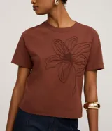 Remera de manga corta color marrón, con cuello redondo y corte recto. Presenta un bordado grande en relieve de una flor en el centro del pecho.