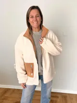 Campera de tejido tipo borrego color crudo, con detalles en pana color camel en bolsillo y cuello interior. De corte oversize y fit relajado, con cierre frontal de cremallera y bolsillos funcionales.