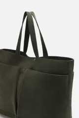 Bolso tipo shopper color verde musgo, confeccionado en cuero con acabado serraje. Tiene compartimento principal con cierre magnético, cuatro bolsillos exteriores y un bolsillo interior con cierre.