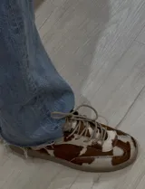 Zapatillas bajas con cordones, de cuero con estampado animal print de vaca en tonos marrón y blanco.