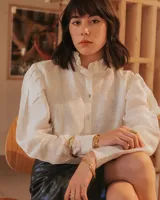 Camisa blanca de lino con cuello con volados y mangas globo abullonadas. Cierre frontal con botones. Corte clásico.