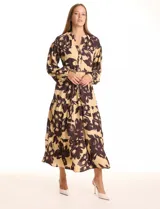 Vestido maxi de crepe estampado con flores grandes en tonos beige y marrón oscuro. Presenta escote en V con botones, mangas largas anchas con botón en los puños, y cintura con pasadores y cordón de ajuste.