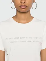 Remera de algodón color blanco con estampa de texto en el frente y manchas negras.