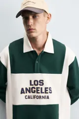 Polo relaxed fit verde oscuro con detalles en blanco, cuello solapa con cierre frontal de botonadura y manga corta. Bordado frontal con la inscripción "Los Angeles California".