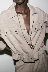 Chaqueta jaspeada color beige, con cuello solapa, manga tres cuartos con trabilla y botón, bolsillos delanteros de plastrón con solapa, bajo ajustable con cordones interiores y cierre frontal con botones a presión.