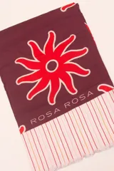 Pareo rectangular de viscosa con estampado de flores rojas sobre fondo borgoña y borde inferior con rayas verticales rojas, amarillas y blancas.