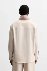 Camisa color crema de corte regular fit, confeccionada en tejido con viscosa. Tiene cuello solapa, manga larga con puños abotonados, bolsillo de parche en el pecho y cierre frontal con botones.