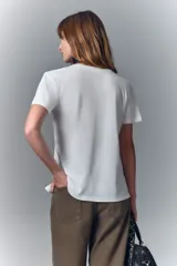 Remera blanca de algodón con cuello redondo y aplique de cadenas metálicas y strass en el escote.