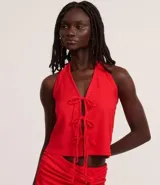 Vestido midi rojo, con textura plisada o arrugada, escote halter en V y detalle de amarras ajustables en el centro del busto que generan una abertura frontal. La falda presenta un fruncido lateral y una abertura alta.