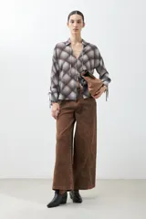 Camisa de manga larga con estampado escocés en tonos chocolate, blanco y gris. Presenta cuello camisero, cierre frontal con lazos y puños con lazos ajustables.