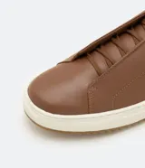 Championes marrones de cuero, con caña baja, ajuste con cordones y suela blanca.