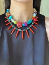Collar corto con cuentas de cerámica, cristales checos y acrílico de diferentes colores y formas. Incluye una concha roja como dije central.