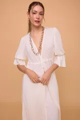 Túnica larga color crudo, confeccionada en lino. Tiene escote en V, mangas 3/4 con volados y elástico, lazos en la cintura y abertura frontal.