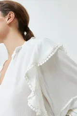 Blusa blanca de bambula con cuello en V y volados en cuello, mangas y frente.