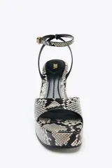 Sandalias de cuña con plataforma y estampado de serpiente en tonos grises y negros. Tira delantera ancha y tira trasera con hebilla metálica. Tacón de 10 cm y punta cuadrada.