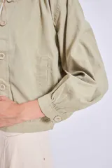Cazadora color verde oliva con cuello redondo, cierre frontal con botones y mangas largas con puños elásticos.