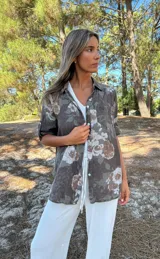 Camisa de algodón color chocolate con estampado floral en tonos beige. Cuenta con cuello camisero, cierre frontal de botones y mangas largas con trabas para arremangar.