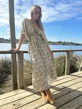 Vestido largo de seda color crema con estampado geométrico en tonos camel y negro. Tiene escote en V, mangas cortas amplias y cintura ajustable con cordón.